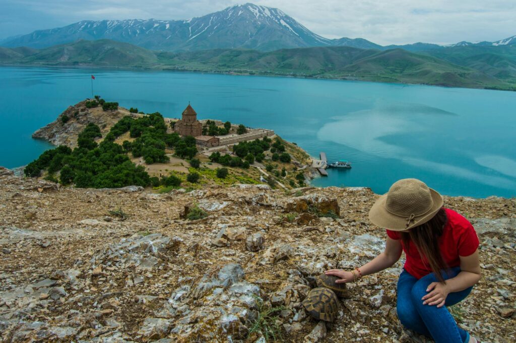 A woman perched on a rock, admiring the tranquil lake and lush greenery in the background.