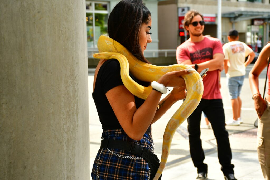 A woman confidently holds a large snake, showcasing her connection with the exotic creature in a natural setting.