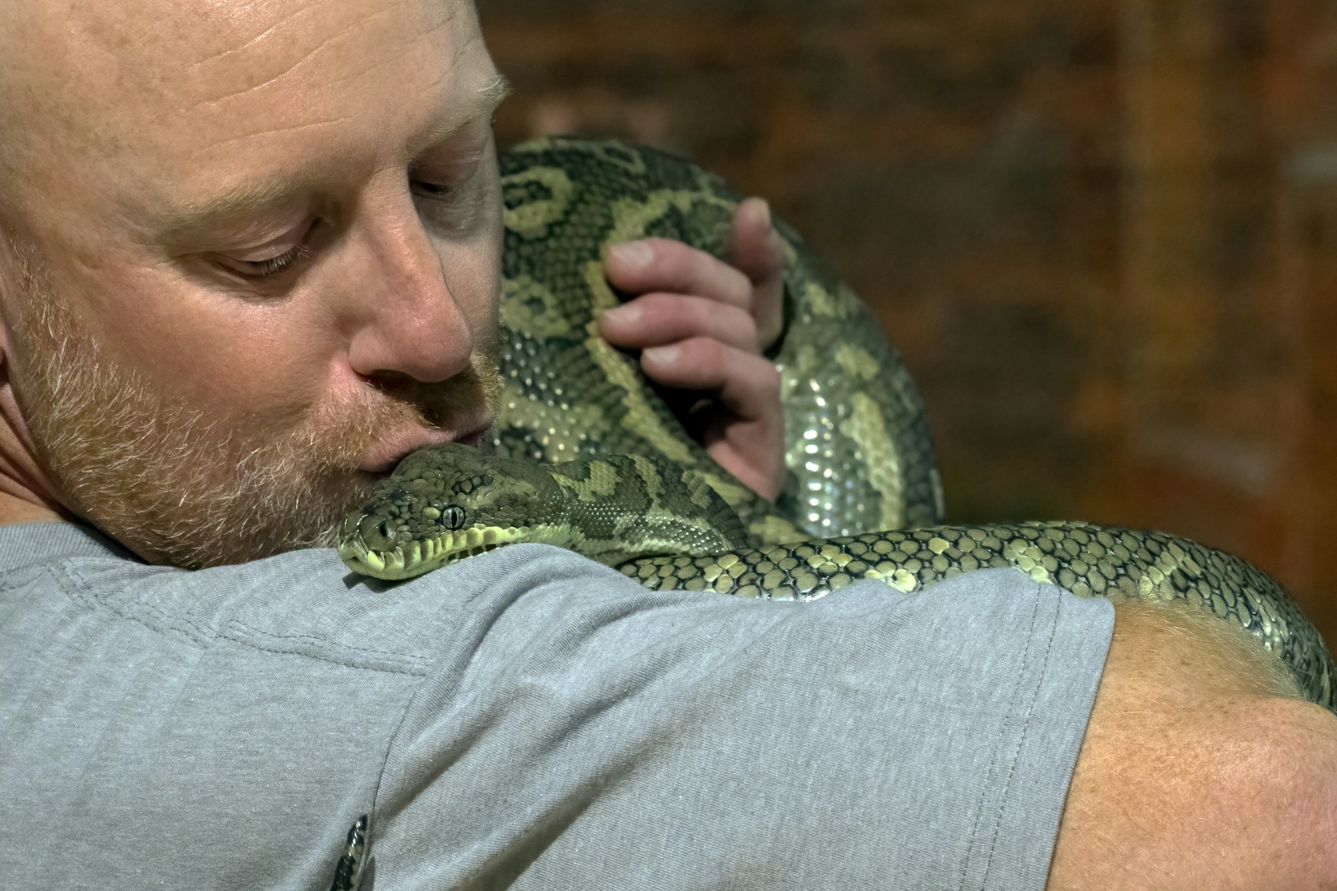 A man cradles a large snake in his arms, showcasing a close bond with the exotic creature.