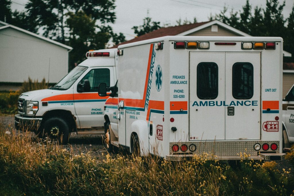 Two ambulances parked in a grassy field beside a residential house, ready for emergency response.
