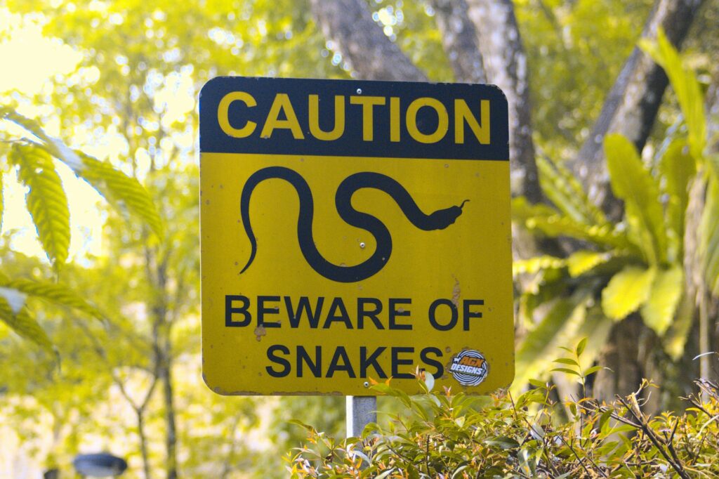A caution sign warning of snakes, featuring a yellow background with black text and a snake graphic.