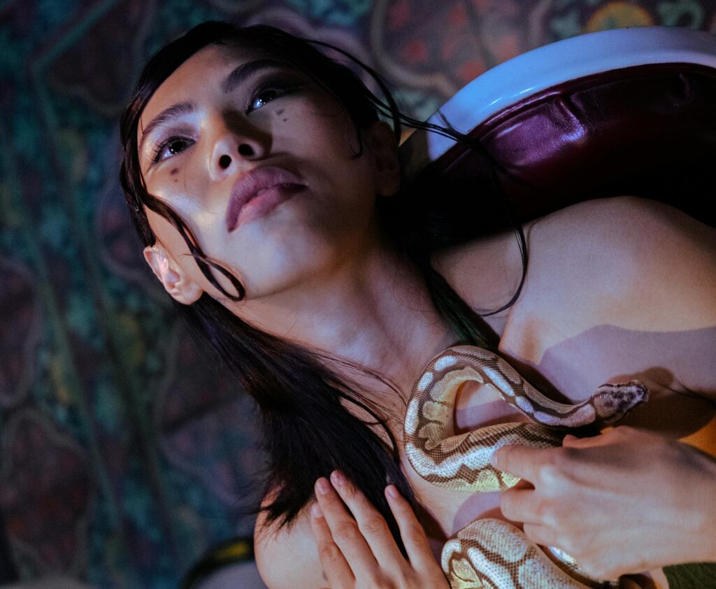 A woman gently cradles a snake in her hands, showcasing her connection with the creature in a serene outdoor setting.